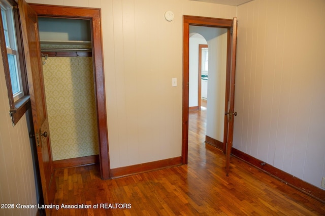 unfurnished bedroom with wallpapered walls, hardwood / wood-style flooring, baseboards, and a closet