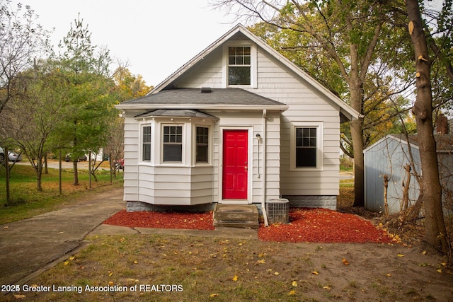 bungalow featuring an outbuilding, central AC unit, and roof with shingles