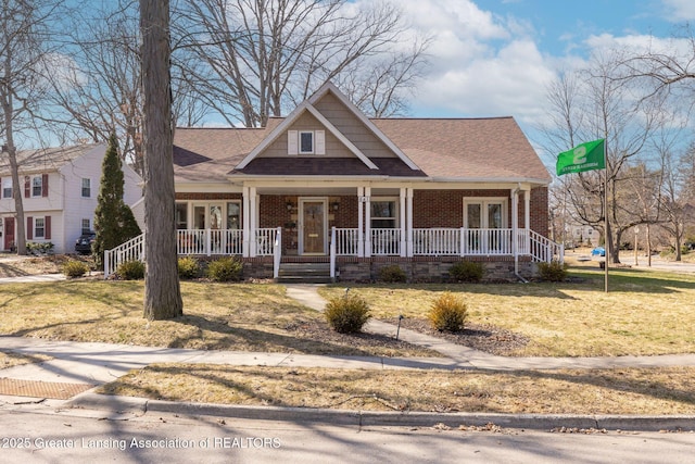 view of front of home with brick siding, covered porch, a front lawn, and roof with shingles