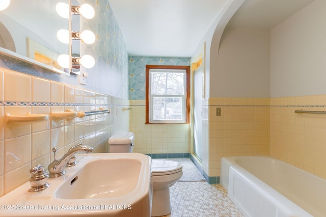 full bath with a bath, a wainscoted wall, a sink, tile walls, and toilet