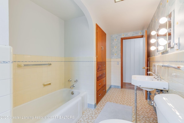 bathroom with tile patterned floors, toilet, wainscoting, a bath, and tile walls