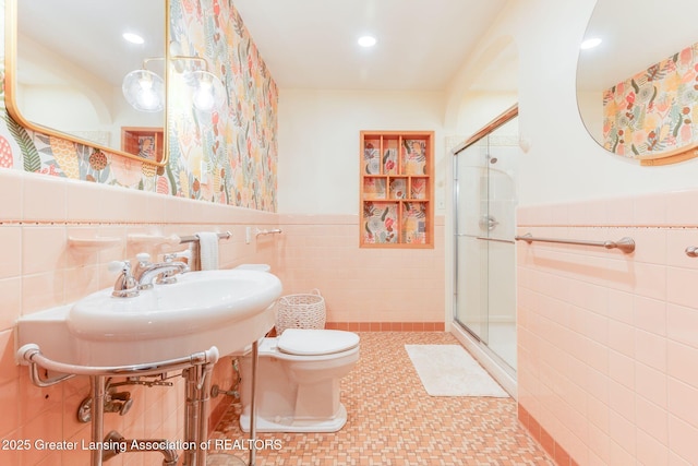 bathroom with a wainscoted wall, toilet, a stall shower, and tile walls