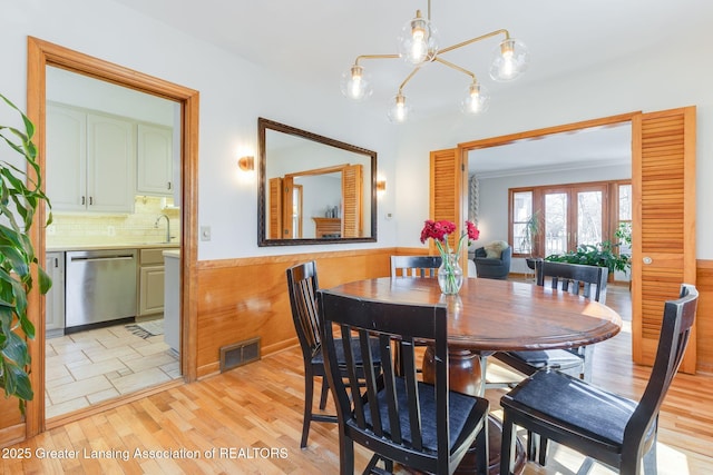 dining space featuring visible vents, wainscoting, light wood-type flooring, and an inviting chandelier