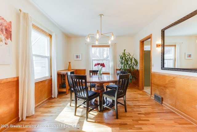 dining space with light wood finished floors, visible vents, wooden walls, a chandelier, and wainscoting