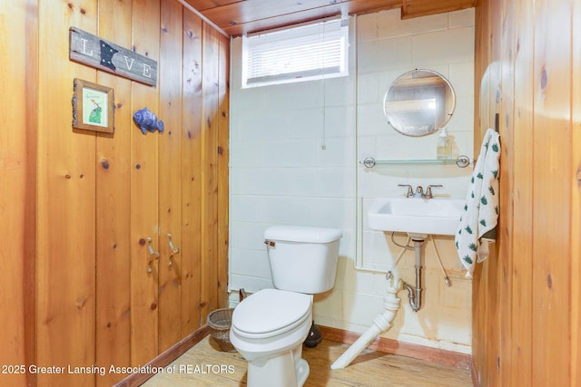 half bath featuring a sink, toilet, wood finished floors, and wood walls