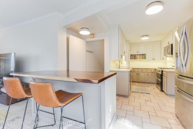 kitchen featuring decorative backsplash, appliances with stainless steel finishes, a breakfast bar area, and crown molding