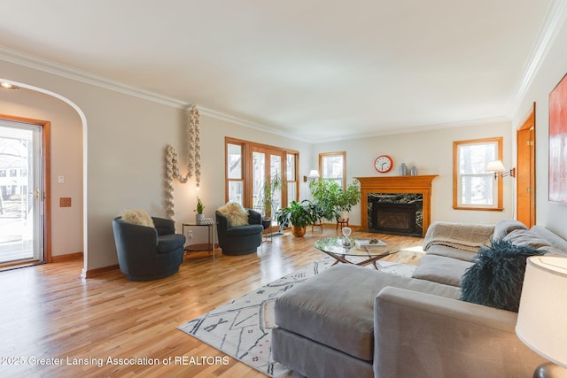 living area featuring a fireplace, arched walkways, light wood finished floors, and ornamental molding