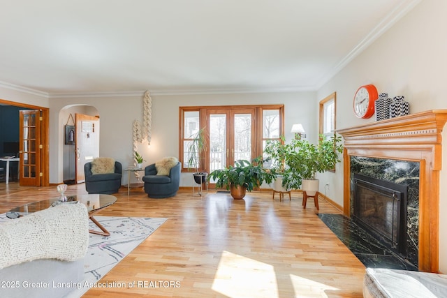 living area with crown molding, wood finished floors, arched walkways, and french doors