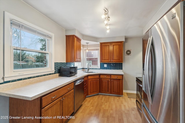 kitchen with a sink, tasteful backsplash, stainless steel appliances, brown cabinetry, and light countertops