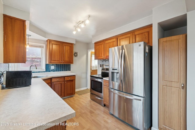 kitchen featuring tasteful backsplash, light countertops, brown cabinets, stainless steel appliances, and a sink