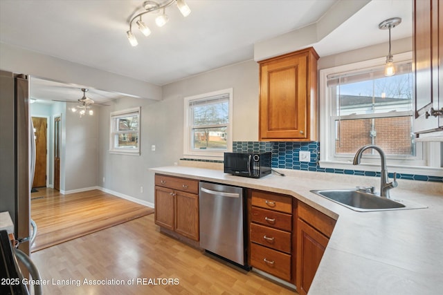 kitchen with a sink, backsplash, stainless steel appliances, brown cabinetry, and light wood finished floors