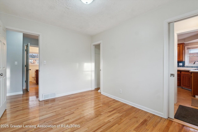 bedroom featuring baseboards, visible vents, light wood finished floors, and a textured ceiling