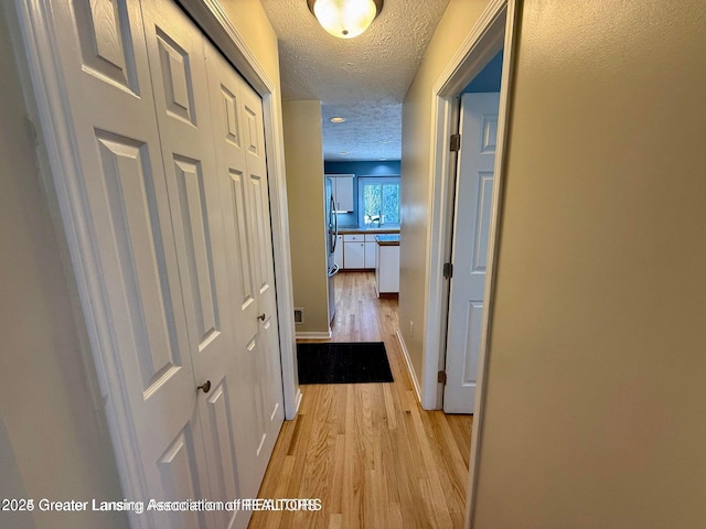 corridor featuring visible vents, light wood-style flooring, a textured ceiling, and baseboards