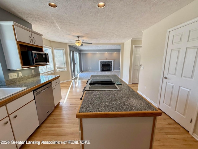 kitchen with ceiling fan, tile countertops, light wood-style flooring, a fireplace, and stainless steel appliances