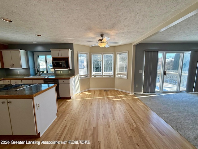 kitchen with baseboards, black microwave, light wood-style floors, white cabinets, and a sink