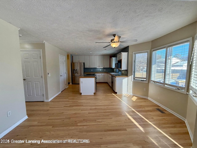 kitchen featuring light wood-style flooring, a sink, a kitchen island, stainless steel appliances, and baseboards