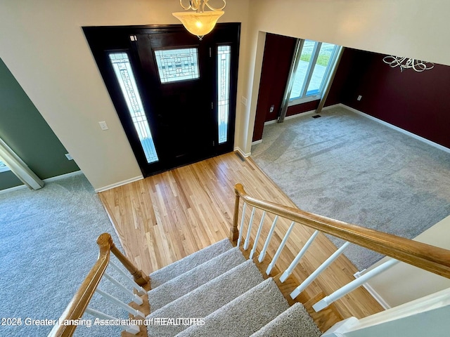 foyer featuring carpet flooring, stairs, baseboards, and wood finished floors