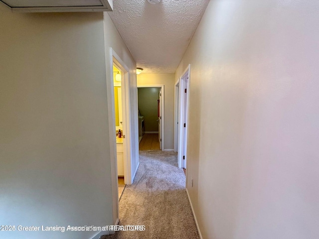 corridor with a textured ceiling, baseboards, and light carpet