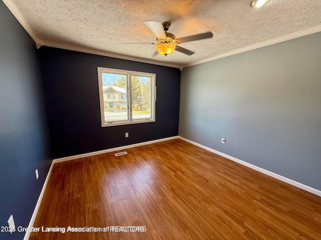 unfurnished room featuring crown molding, wood finished floors, visible vents, and baseboards