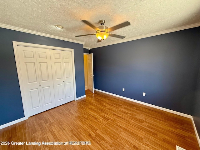 unfurnished bedroom with baseboards, wood finished floors, a closet, and ornamental molding