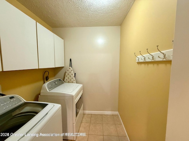 washroom featuring light tile patterned floors, baseboards, cabinet space, a textured ceiling, and washer and clothes dryer