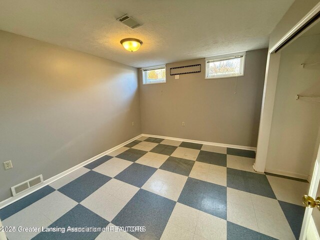 basement with tile patterned floors, visible vents, baseboards, and a textured ceiling