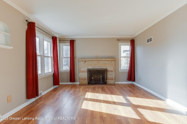 unfurnished living room with a stone fireplace, wood finished floors, visible vents, and ornamental molding