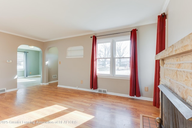 unfurnished living room with light wood-style floors, a fireplace, arched walkways, and visible vents