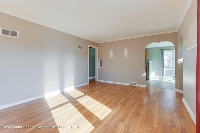 empty room with arched walkways, visible vents, and light wood finished floors