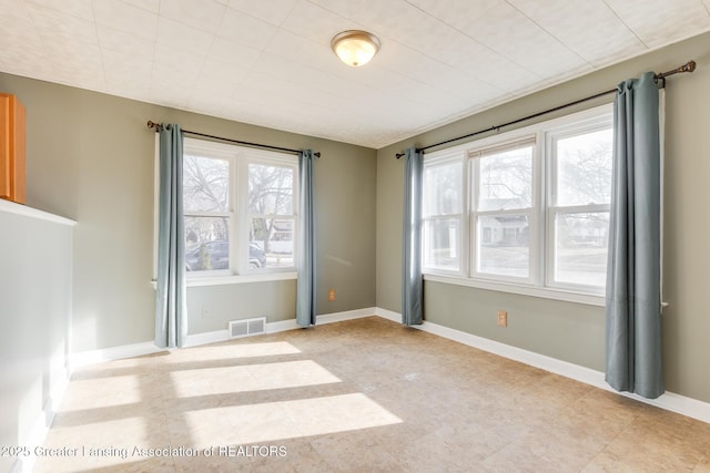 unfurnished room featuring a healthy amount of sunlight, visible vents, and baseboards