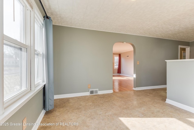 spare room featuring visible vents, arched walkways, and baseboards