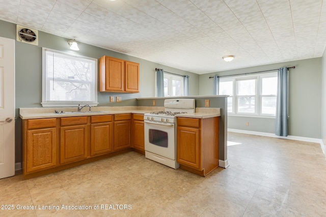 kitchen with gas range gas stove, light countertops, a peninsula, brown cabinetry, and a sink