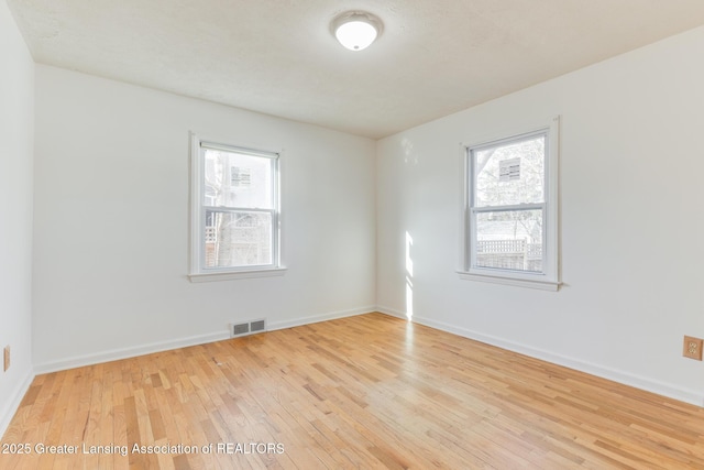 spare room featuring a wealth of natural light, visible vents, baseboards, and light wood-style floors