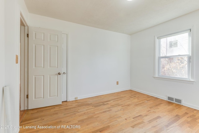 empty room with light wood-style floors, visible vents, and baseboards