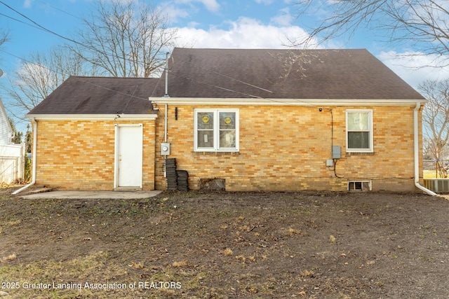 rear view of house featuring brick siding and roof with shingles