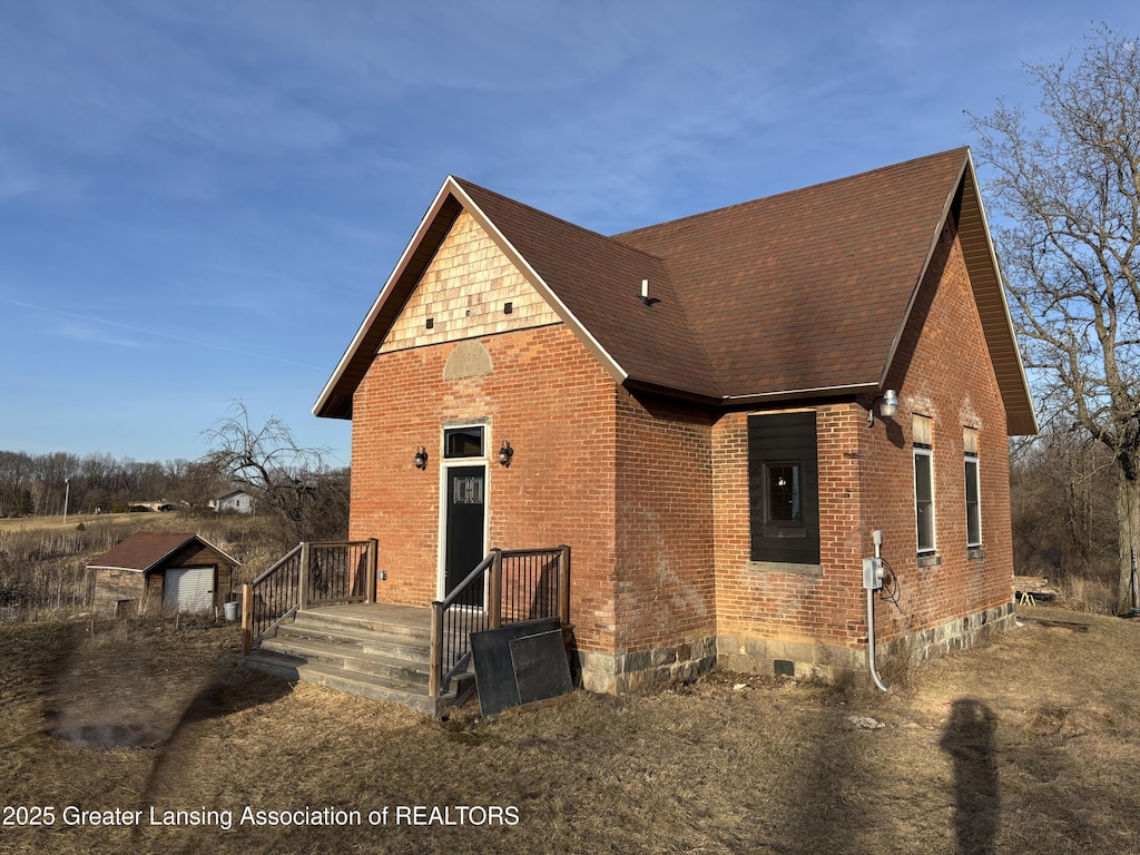 view of front facade featuring brick siding, an outdoor structure, and roof with shingles