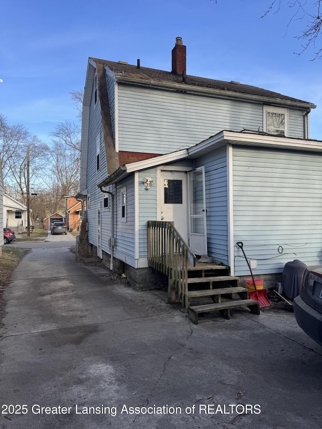 rear view of house with entry steps, a chimney, and driveway