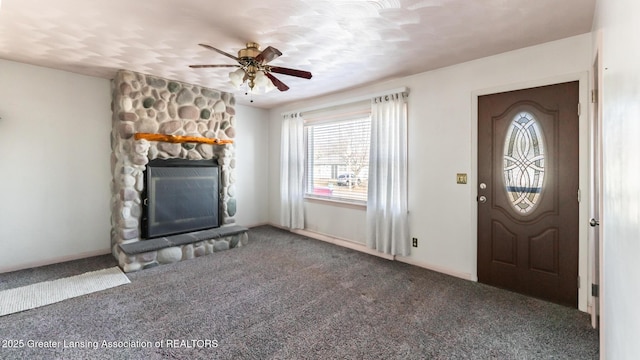 foyer entrance featuring baseboards, a ceiling fan, a stone fireplace, and carpet flooring