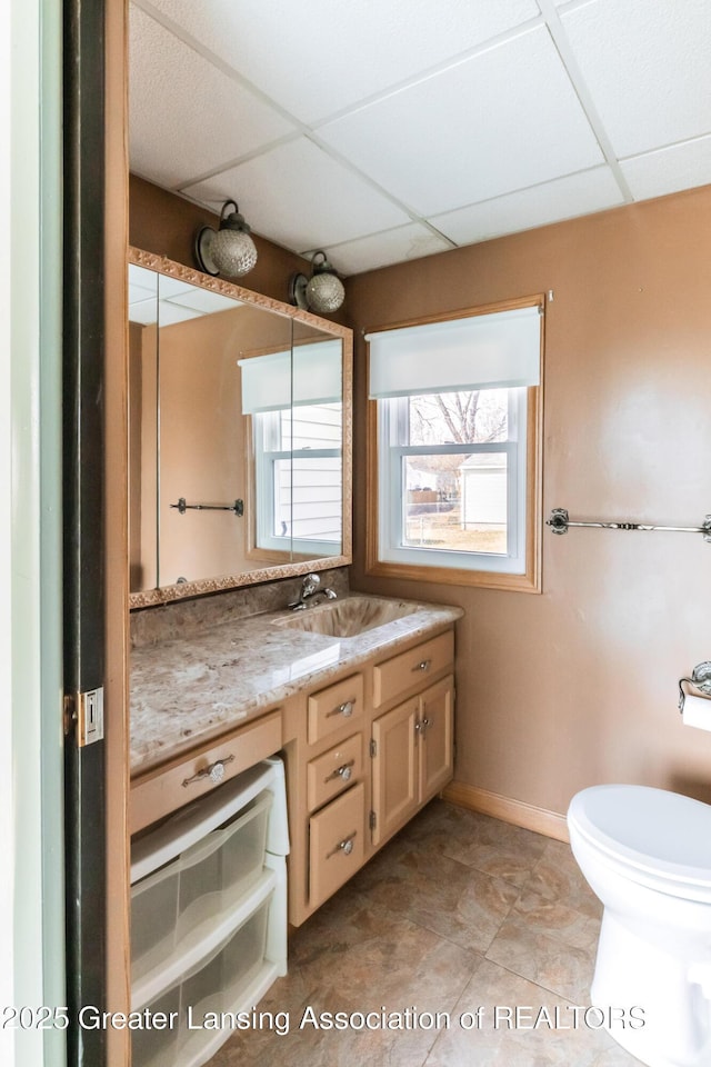 bathroom featuring vanity, toilet, baseboards, and a drop ceiling