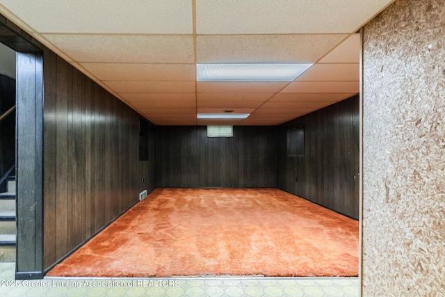 finished basement featuring visible vents, a paneled ceiling, wooden walls, and carpet