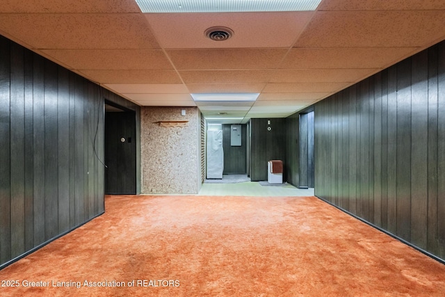 interior space featuring carpet, wooden walls, a paneled ceiling, and visible vents