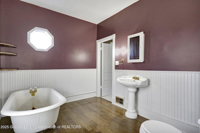 full bath featuring a freestanding tub, a wainscoted wall, toilet, visible vents, and wood finished floors