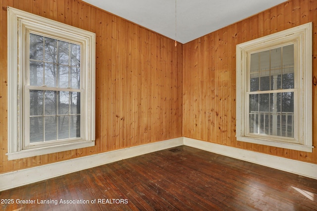 unfurnished room featuring baseboards, wood walls, and dark wood-style flooring