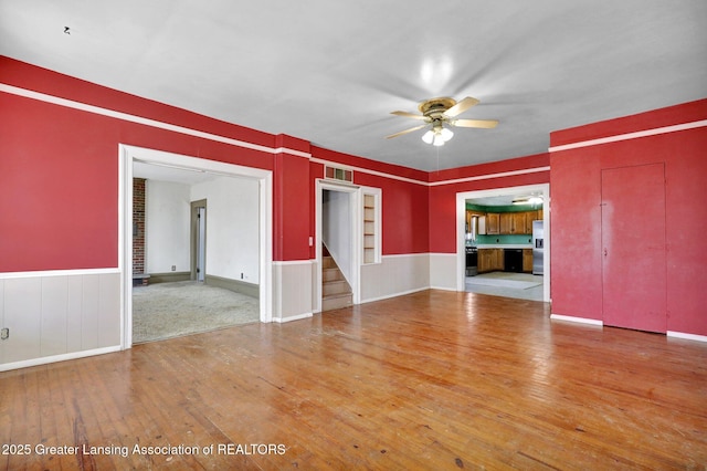 spare room featuring visible vents, a ceiling fan, stairway, wood-type flooring, and wainscoting