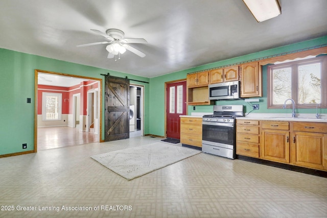 kitchen with a sink, a barn door, appliances with stainless steel finishes, light countertops, and light floors