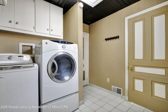 washroom with visible vents, wooden walls, washer and clothes dryer, light tile patterned flooring, and cabinet space