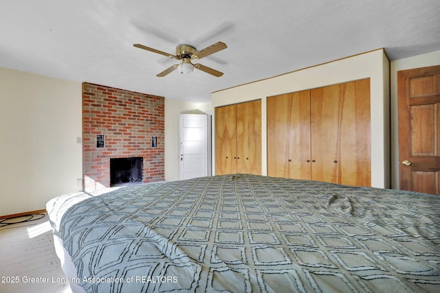 bedroom featuring baseboards, multiple closets, a fireplace, wood finished floors, and a ceiling fan