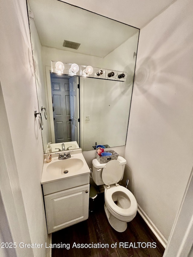 half bathroom with visible vents, toilet, wood finished floors, baseboards, and vanity