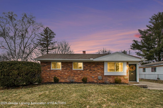 view of front of property featuring brick siding, a chimney, a front lawn, and a shingled roof