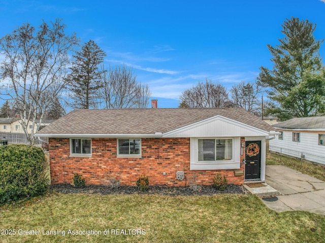 ranch-style home featuring a front yard, brick siding, roof with shingles, and a chimney